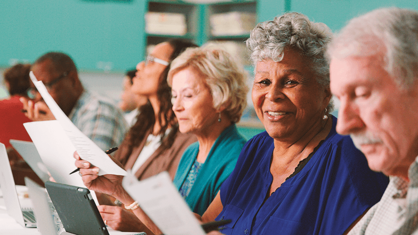 smiling older adults looking at papers in a classroom