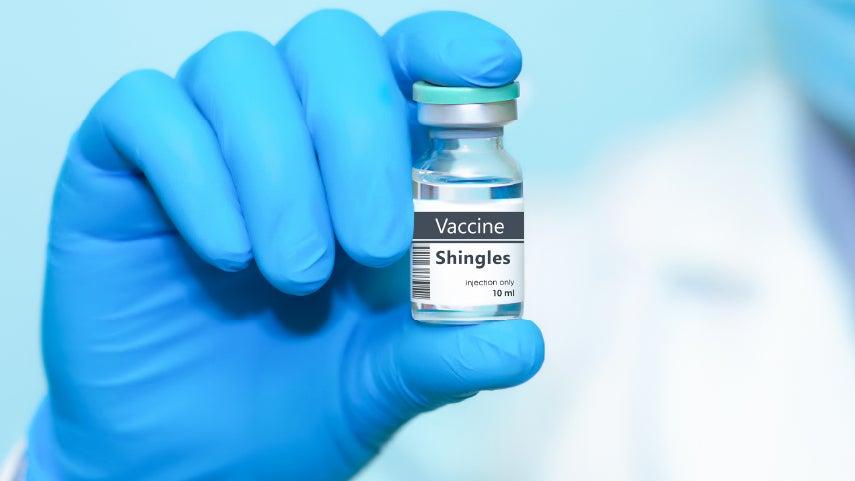 Close up of a Shingles vaccine vile held in a doctor's hand, who is wearing blue latex gloves.
