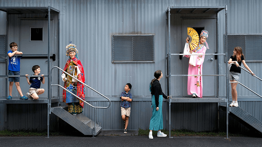Children and older adults dressed in ceremonial Chinese attire stand together on stairs