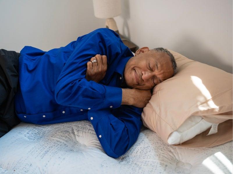 A man in a bright blue shirt lies on his side on the Serta Perfect Sleeper mattress