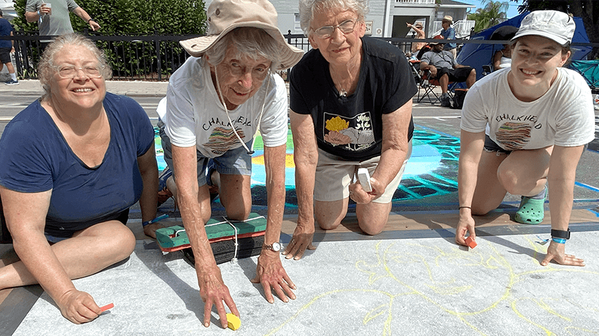 four women of different ages drawing with sidewalk chalk
