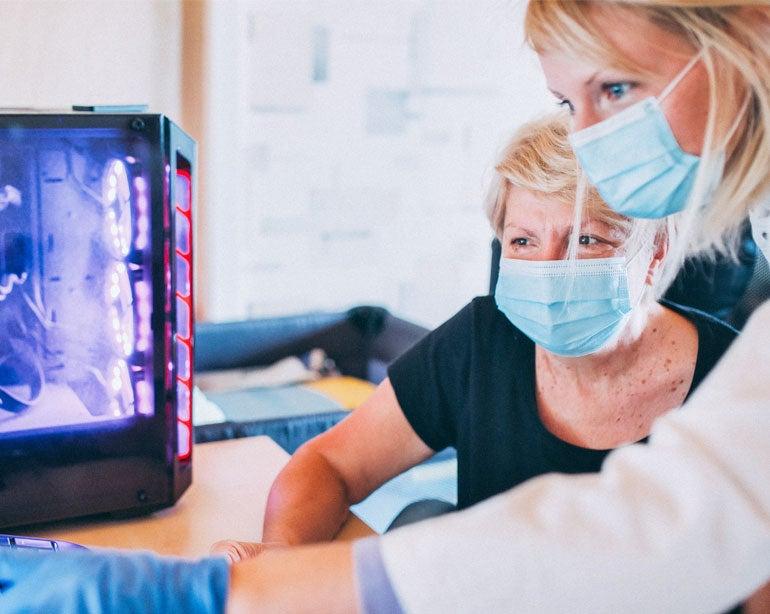 A senior woman wearing a mask is reviewing her chronic condition with her younger female doctor.