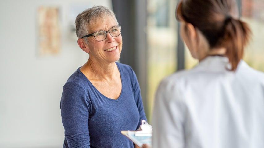 older woman smiling and facing a woman in a lab coat with a clipboard