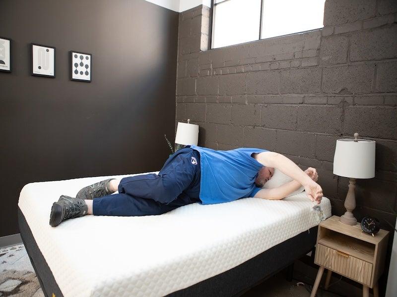 A man in a blue shirt changes sleeping positions on the Nolah All-Foam mattress