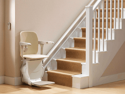 A Stannah stair lift waiting at the bottom of a set of indoor stairs