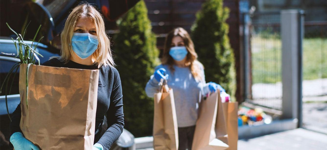 Two women spaced six feet apart are delivering groceries to a senior's home during the pandemic.