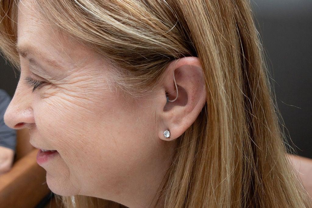 A woman shown from the side wearing a hearing aid in her left ear