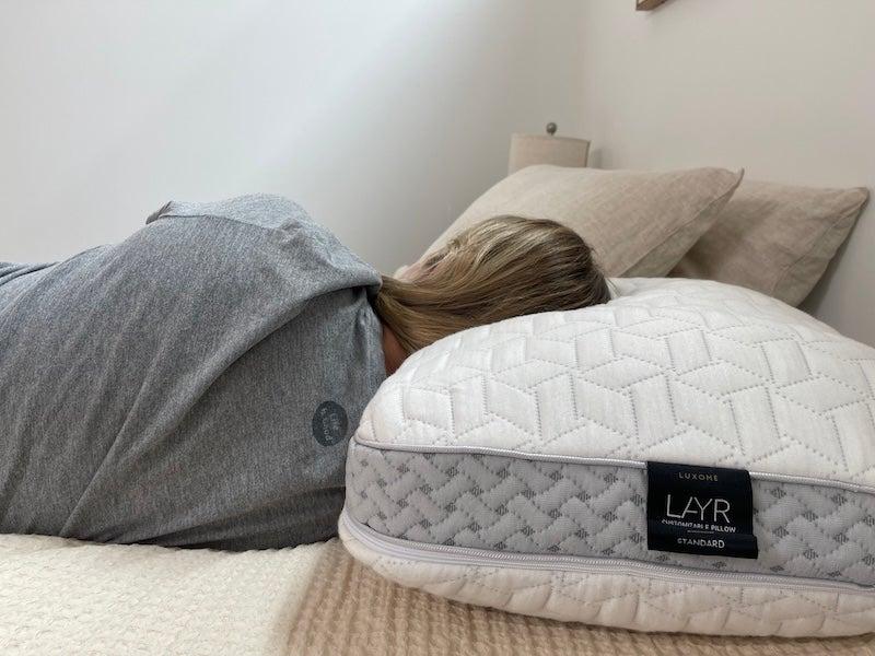 A woman lies on her side on the Luxome LAYR pillow.