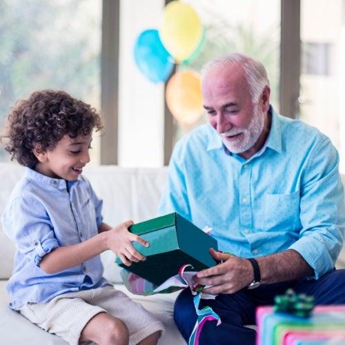 An older man and a young boy sitting on a couch unwrapping a gift