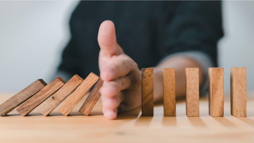 wood blocks falling over and a hand preventing more from falling