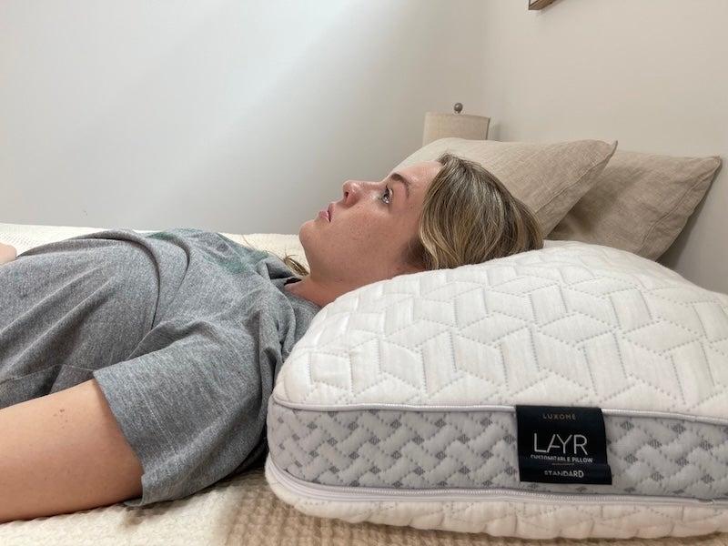 A woman lies on her back on the Luxome LAYR pillow.