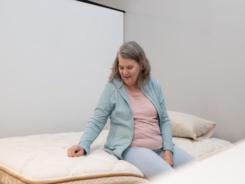A woman sits on the edge of the Saatva Solaire adjustable mattress