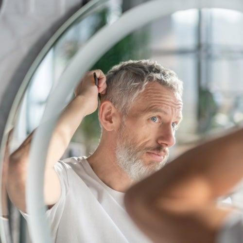 A man looks into a mirror and combs his short white hair.