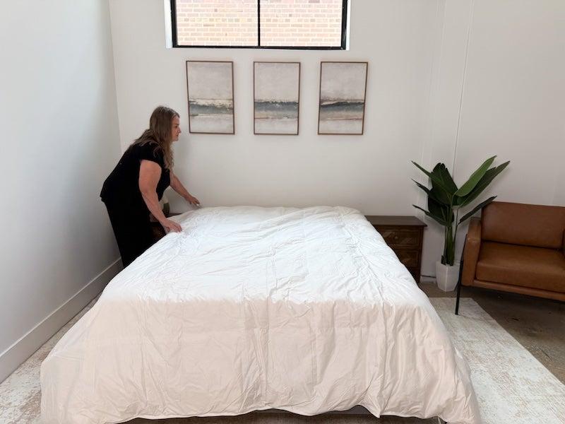 A tester smooths out the Brooklinen Down Comforter onto a bed.