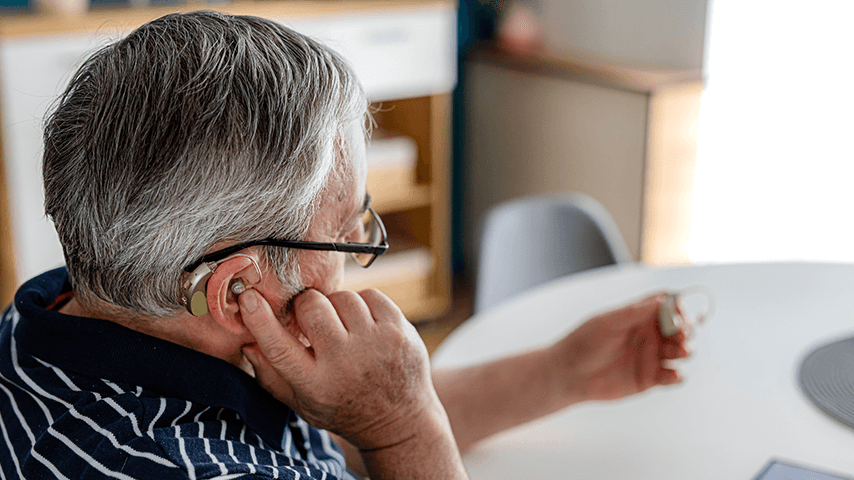 older man holding a hearing aid in left hand while placing one in right ear
