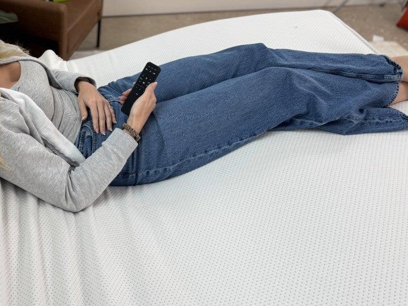 A woman lying on the Helix Adjustable base holding its remote