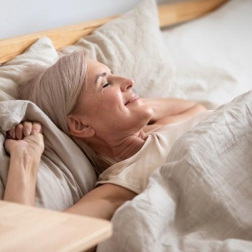 A woman lying in bed, looking like she’s just waking up, with a small smile