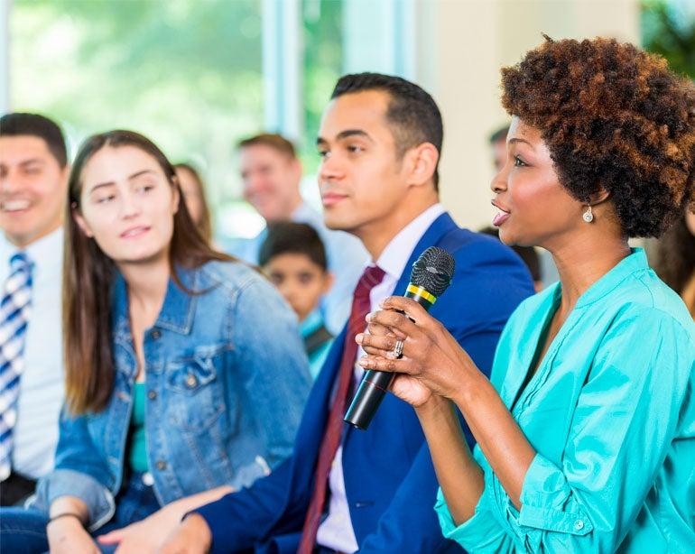A professional advocating on behalf of older adults is holding a mic, asking a question at a town hall.