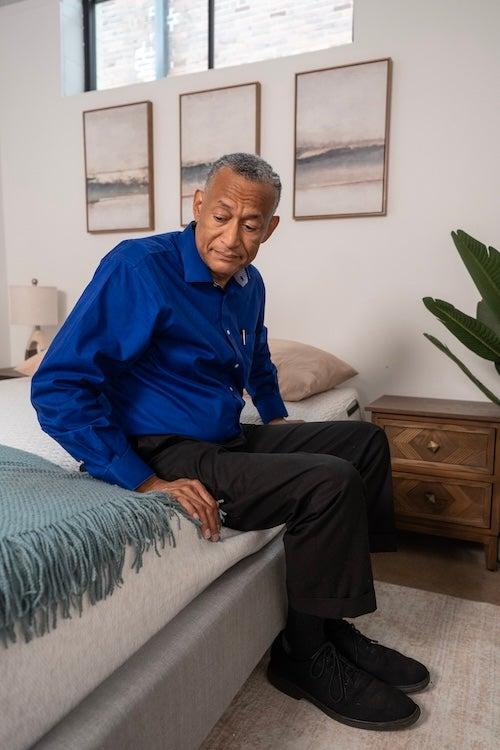 A man in a cobalt blue shirt sits on the edge of the Tuft & Needle Original Mattress to demonstrate edge sinkage