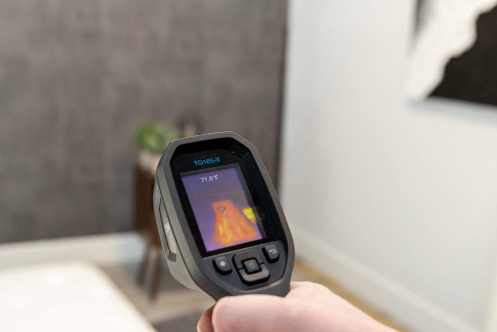 A person holding a heat gun in their right hand, pointing it at a mattress