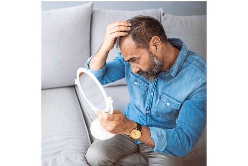 A man sitting on a couch looking at his hairline in a mirror