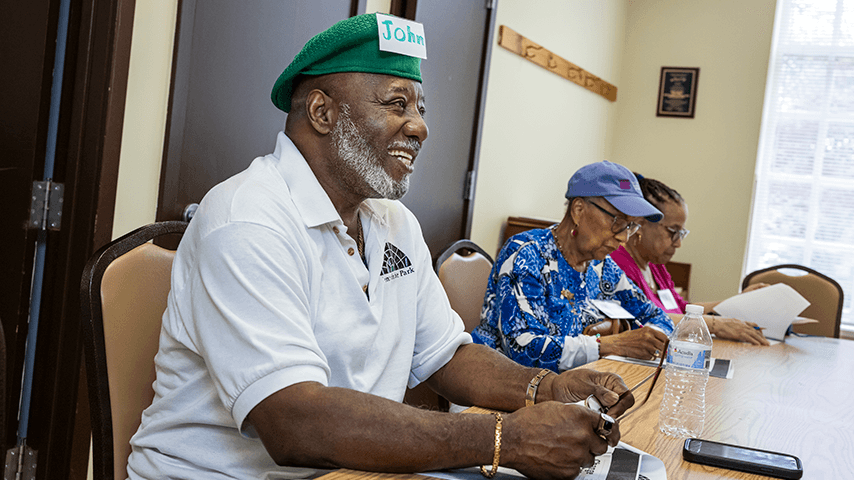 Smiling older man at table with two older women looking at papers
