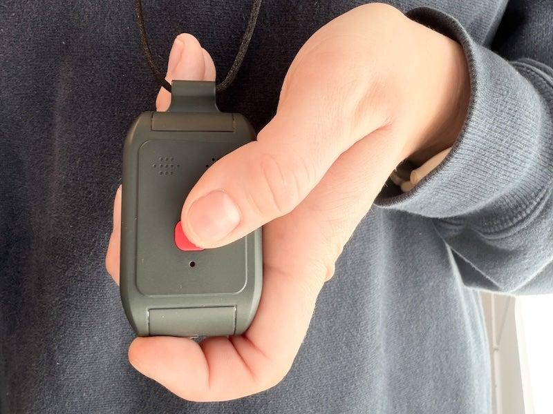 Person in grey sweater holding the red help button on the Alert1 LifeBeacon