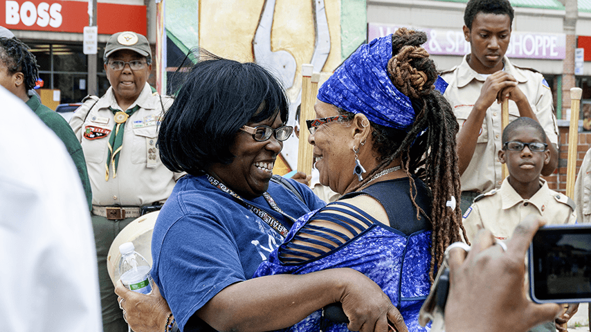 grinning women embracing with Boy Scouts in background