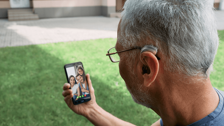 gray-haired man wearing hearing aid holding cellphone with image of three family members on phone