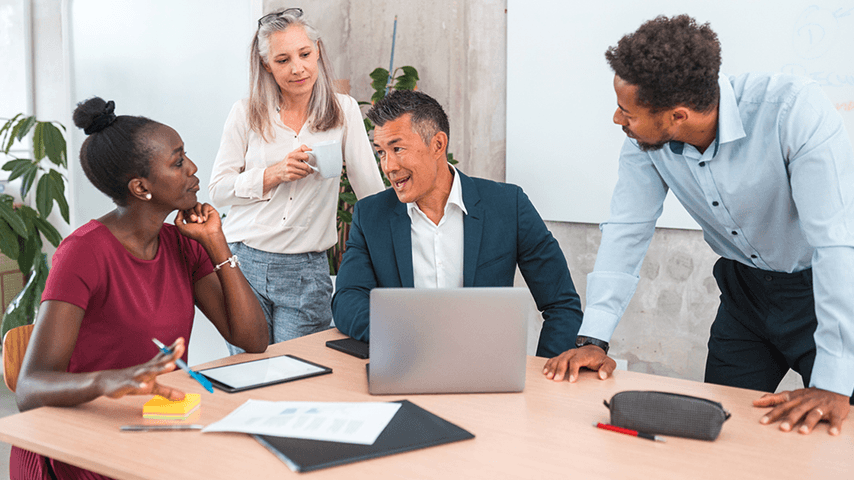 four office workers gathered around a laptop