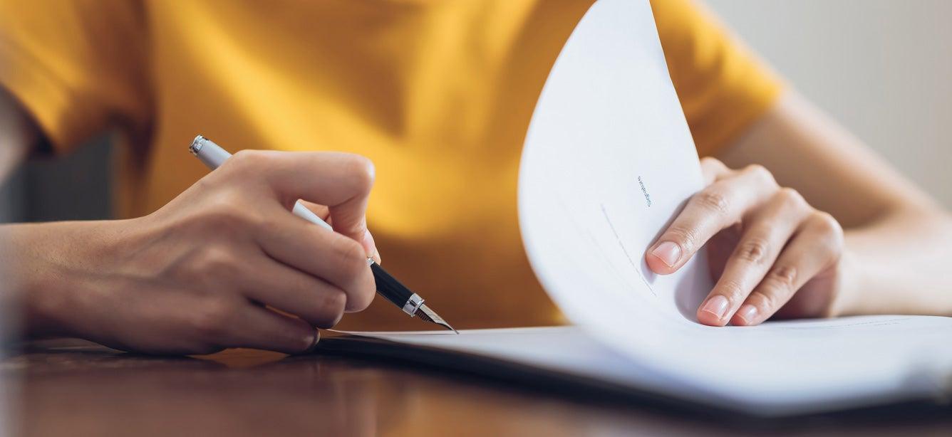 A woman wearing a yellow shirt is signing an important document.
