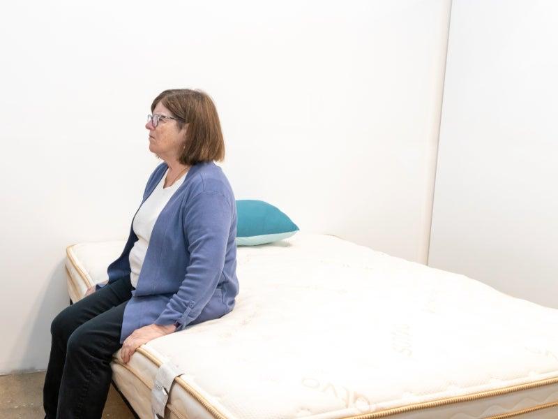 A woman sitting on the edge of the Saatva Classic mattress