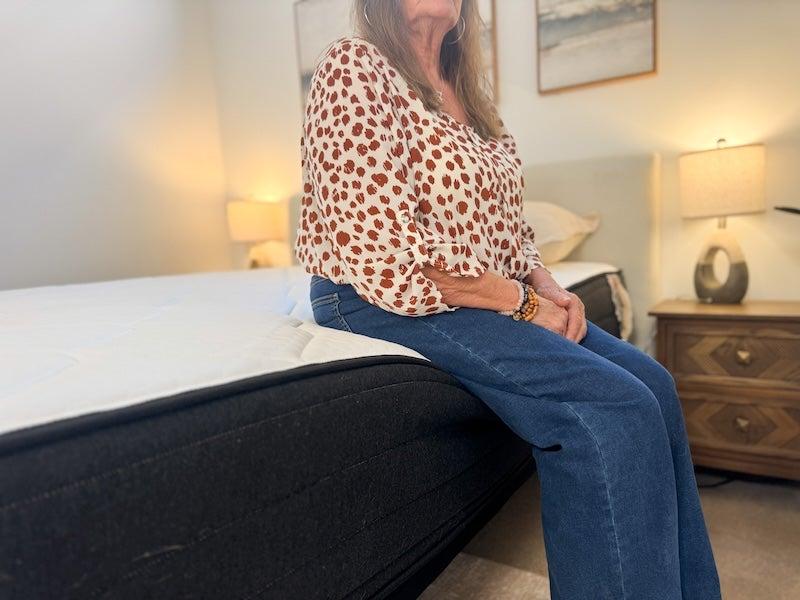 A woman sits on the edge of a Plank Firm mattress