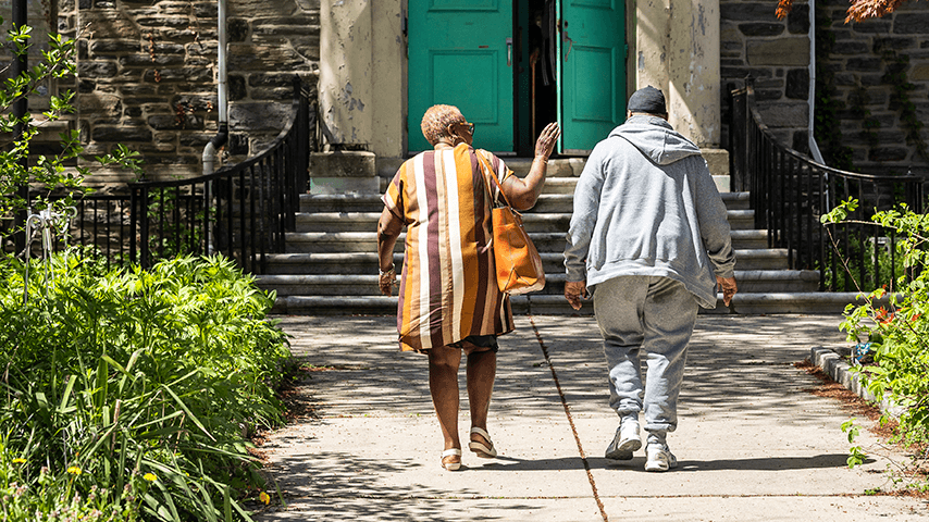 older man and woman walking toward front steps of a senior center