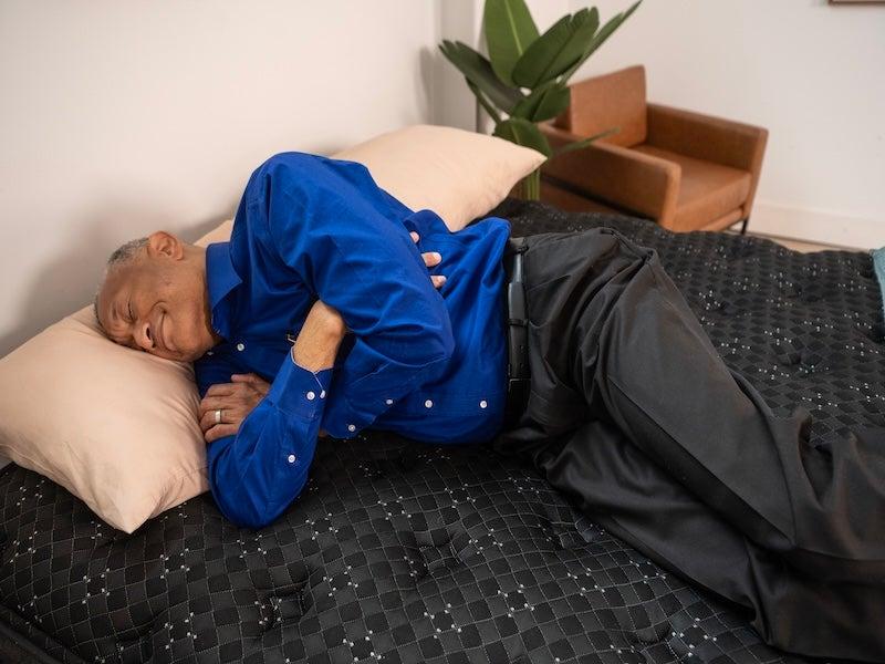 A man in a cobalt blue shirt changes positions on top of the Beautyrest Black mattress