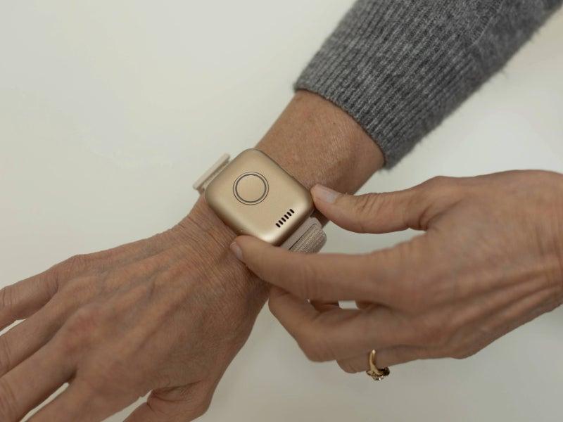 The gold Guardian Flex worn as a wristband on the arm of a woman wearing a grey sweater