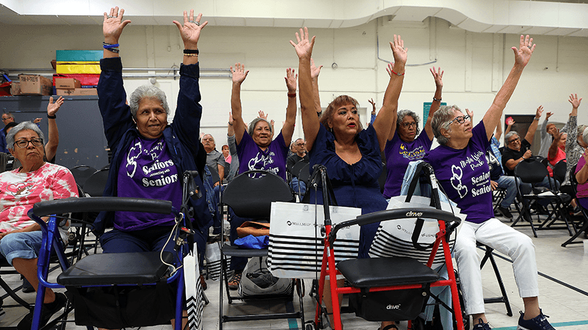 room full of seated older adults with arms raised during falls prevention exercise