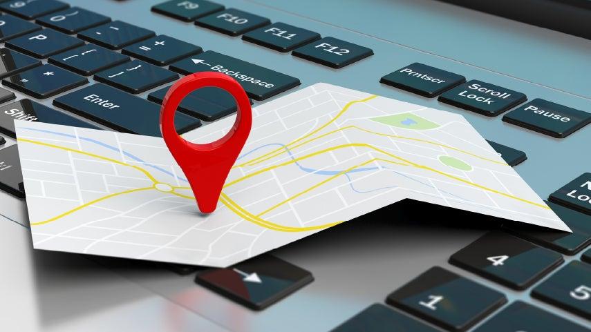 A map is sitting on top of a computer with a pinpoint in the center of the map.
