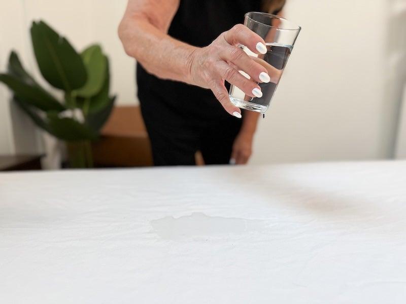 A woman pours a glass of water on a mattress covered by the Helix Waterproof Mattress Protector
