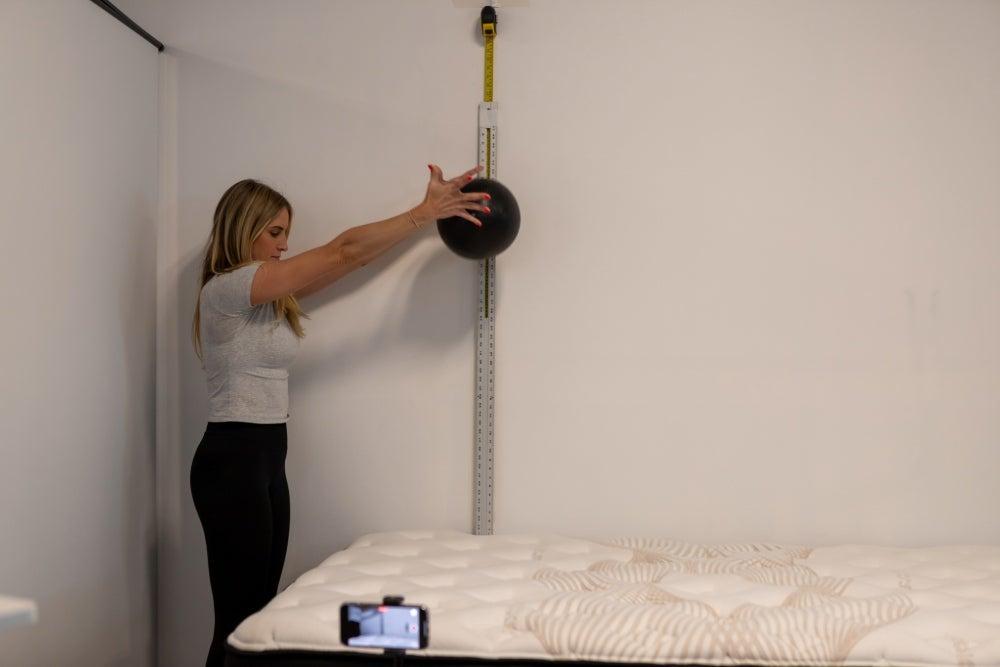 A woman dropping a weighted ball onto the Nolah Evolution Luxury Firm mattress