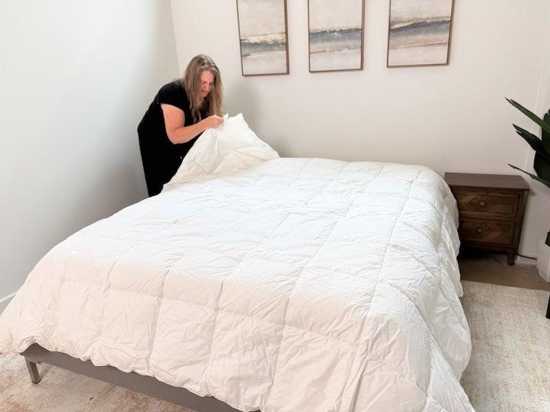 A tester spreads the Silk & Snow Down Alternative Comforter out onto a bed.