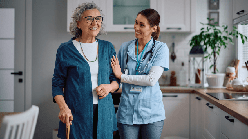 A younger assisted living worker is helping an older adult woman walk.