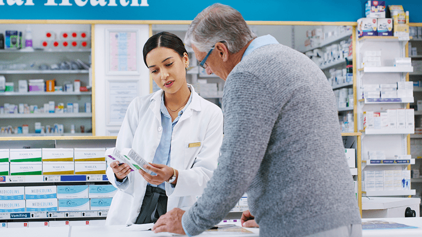 pharmacist talking to older man at pharmacy counter