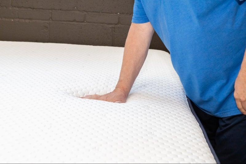 A man pressing his hand into the Brooklyn Bedding Aurora Luxe Cooling mattress