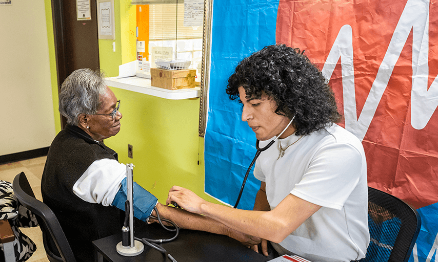young Hispanic man checks blood pressure of older black woman