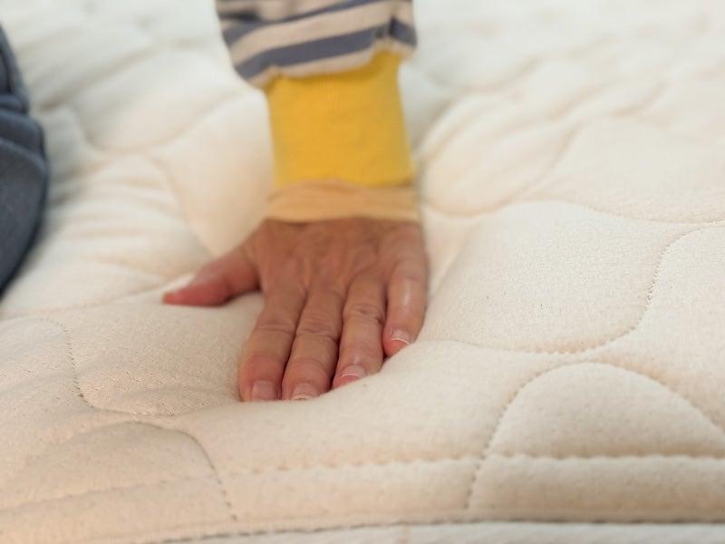 A woman presses down on the top of the WinkBed EcoCloud latex hybrid mattress.