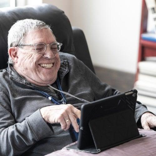 A man with oxygen tubing in his nose laughing at something on a tablet.