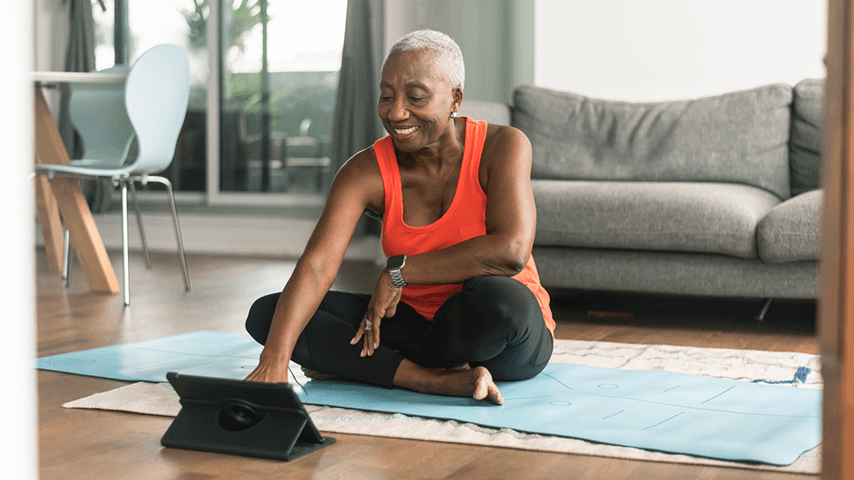 smiling older woman on yoga mat looking at tablet