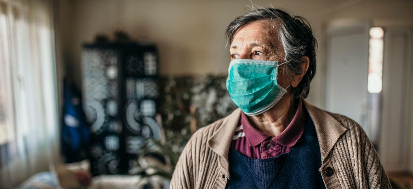 A senior woman is at home, sheltering in place and wearing a mask.
