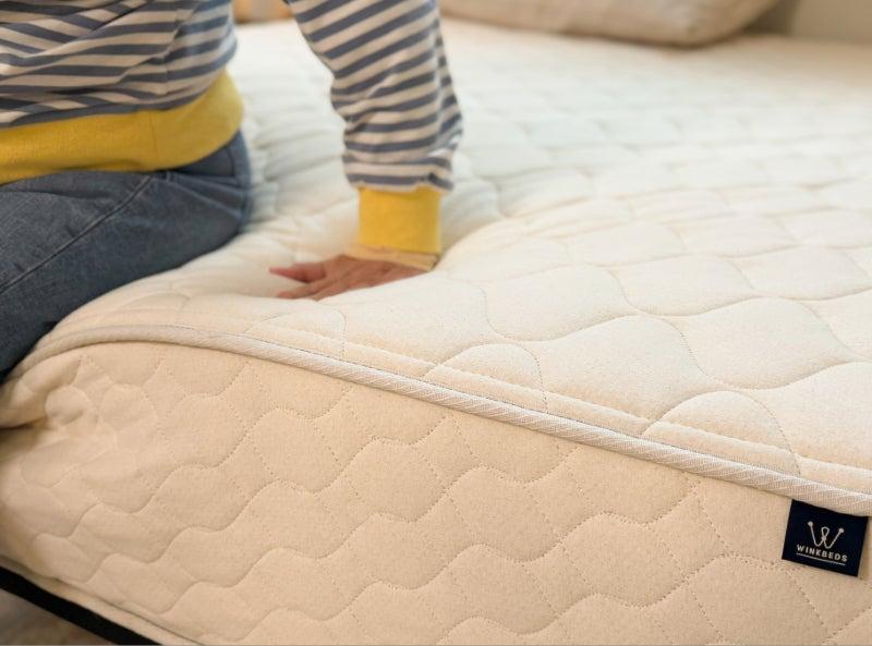 A person sitting on the edge of the WinkBed EcoCloud mattress